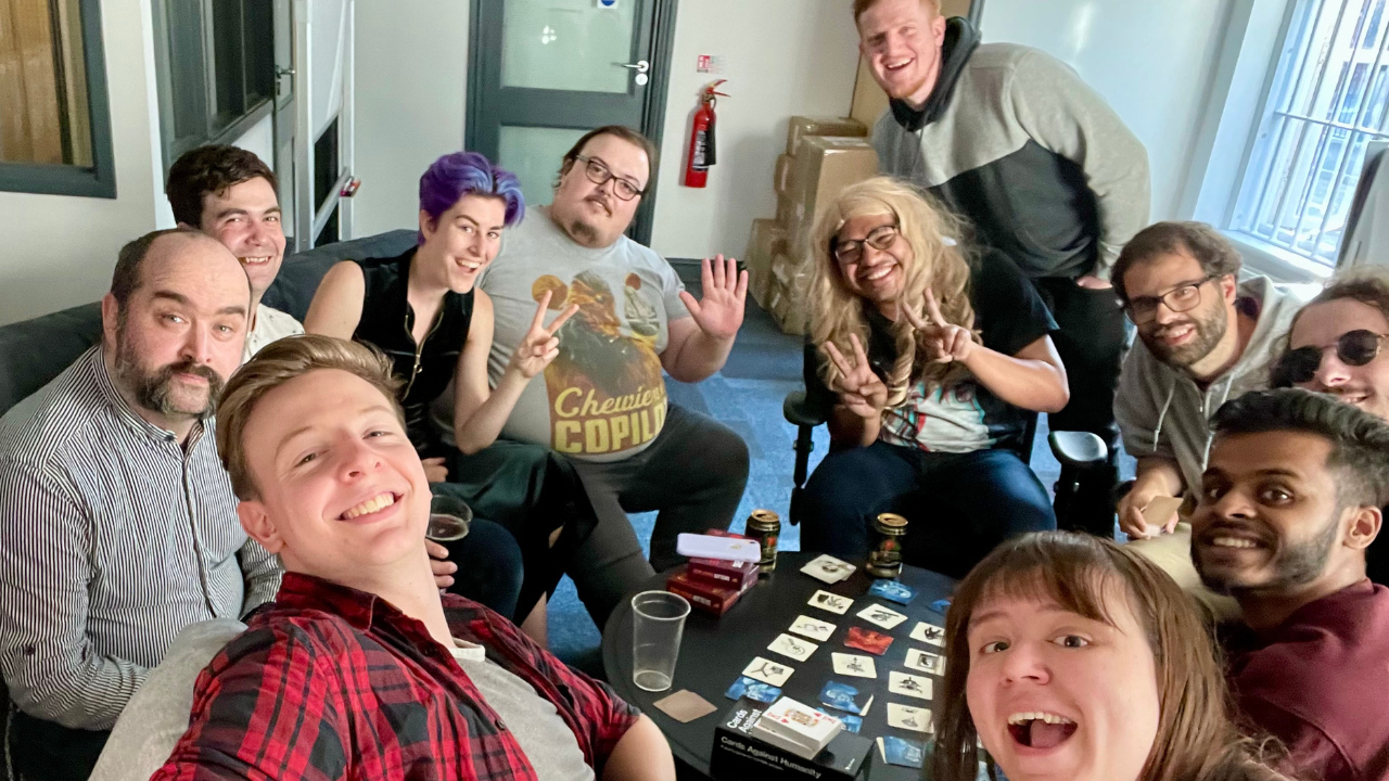 A group of smiling people sitting around a tabletop card game